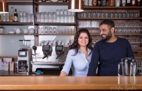 Zwei Personen lächeln hinter einer Café-Bar mit Espressomaschine., © Donauhhof